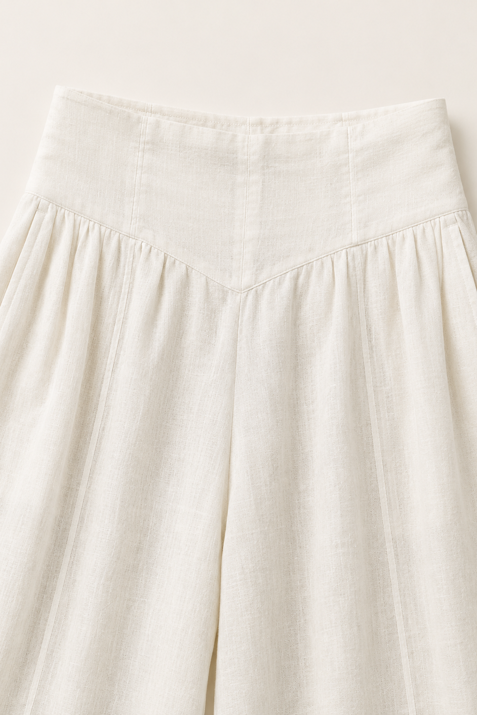 Close-up of a high-waisted, wide-leg skirt in a textured off-white linen fabric, showing the waistband and pleated front panel.