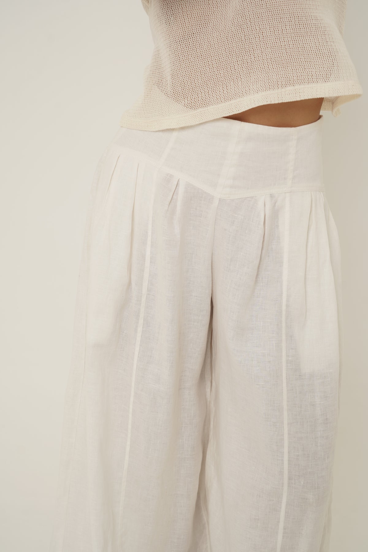 Woman wearing a white linen pants with a transparant knitted top. 