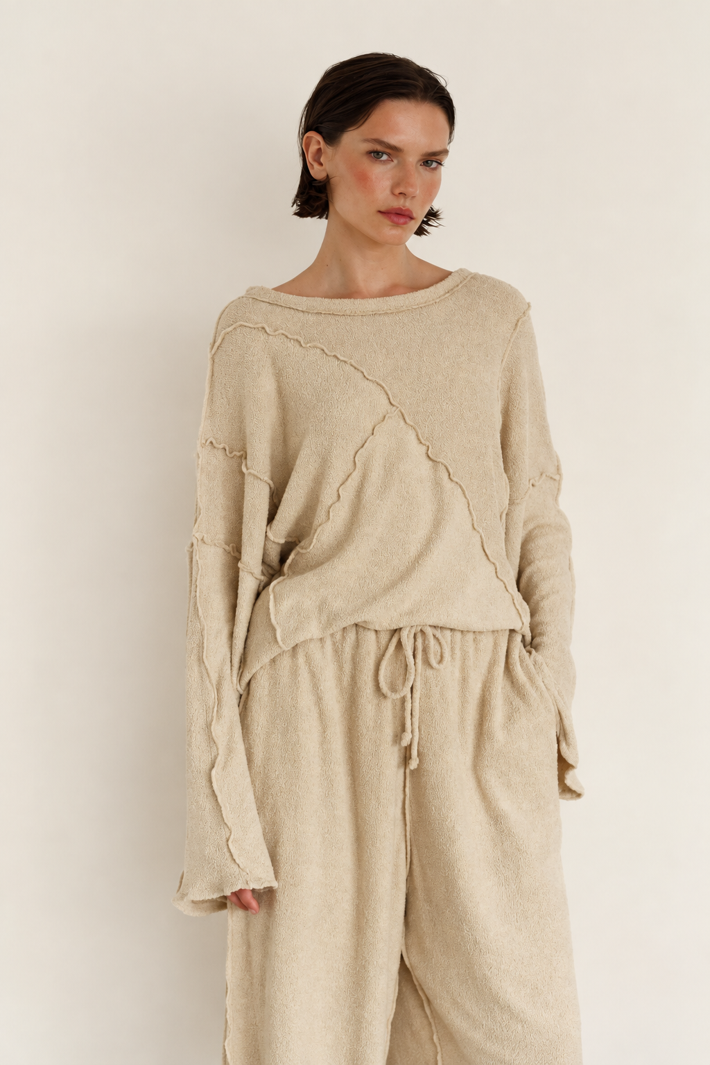 A model wearing a beige knit sweater and matching drawstring pants against a plain off-white background.