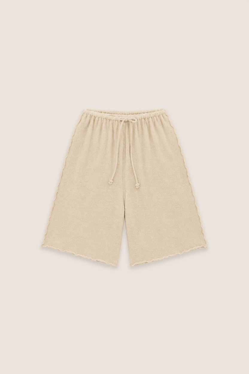 Beige knit shorts with a drawstring waist and raw, frayed hems, laid flat on a light beige background.