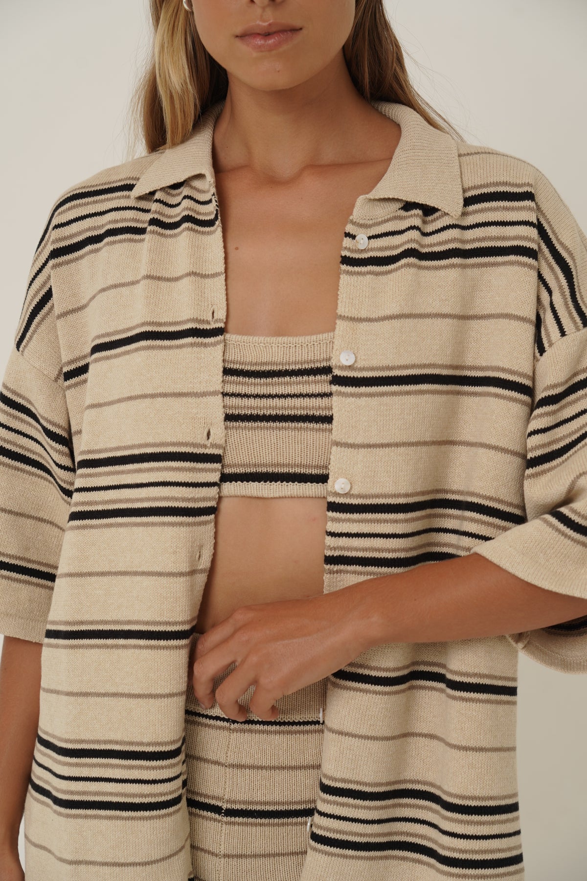 A close-up of a model wearing a beige knit cardigan with black and dark brown vertical stripes, styled open over a matching striped top.