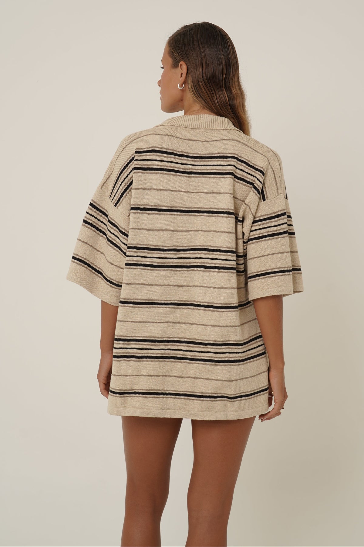 A model wearing a cream-colored short-sleeve top with thin black vertical stripes, shown from a side profile against a plain light beige background.