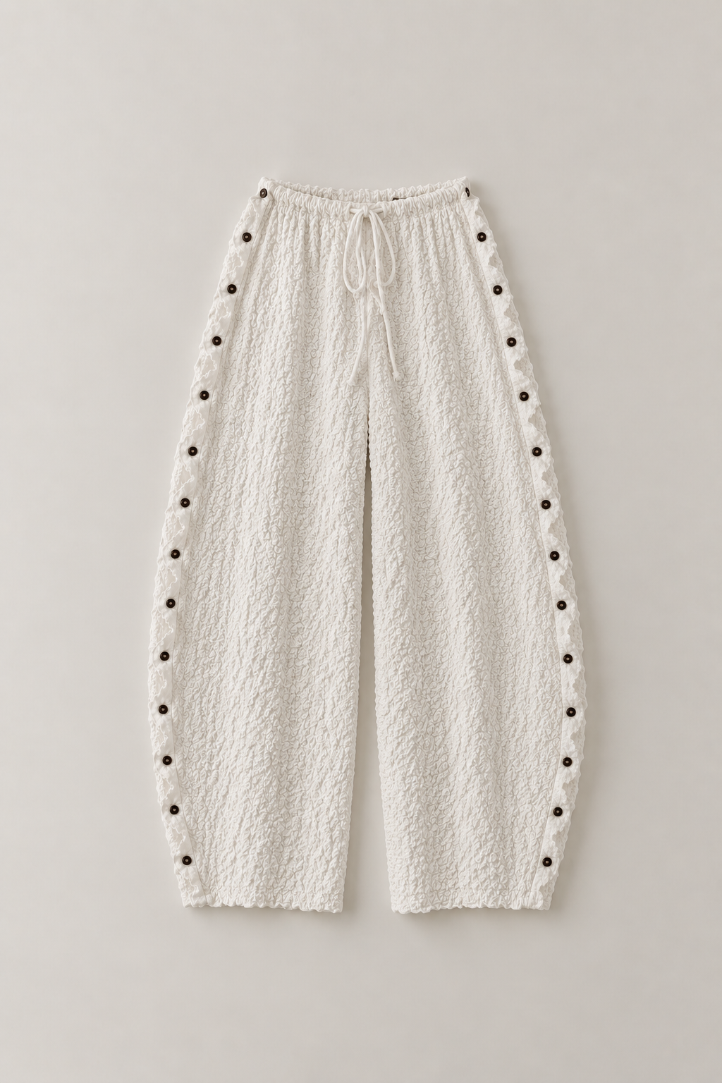 Cream textured wide-leg pants with a drawstring waist and rows of decorative dark buttons down the outer sides, shown flat on a light gray background.
