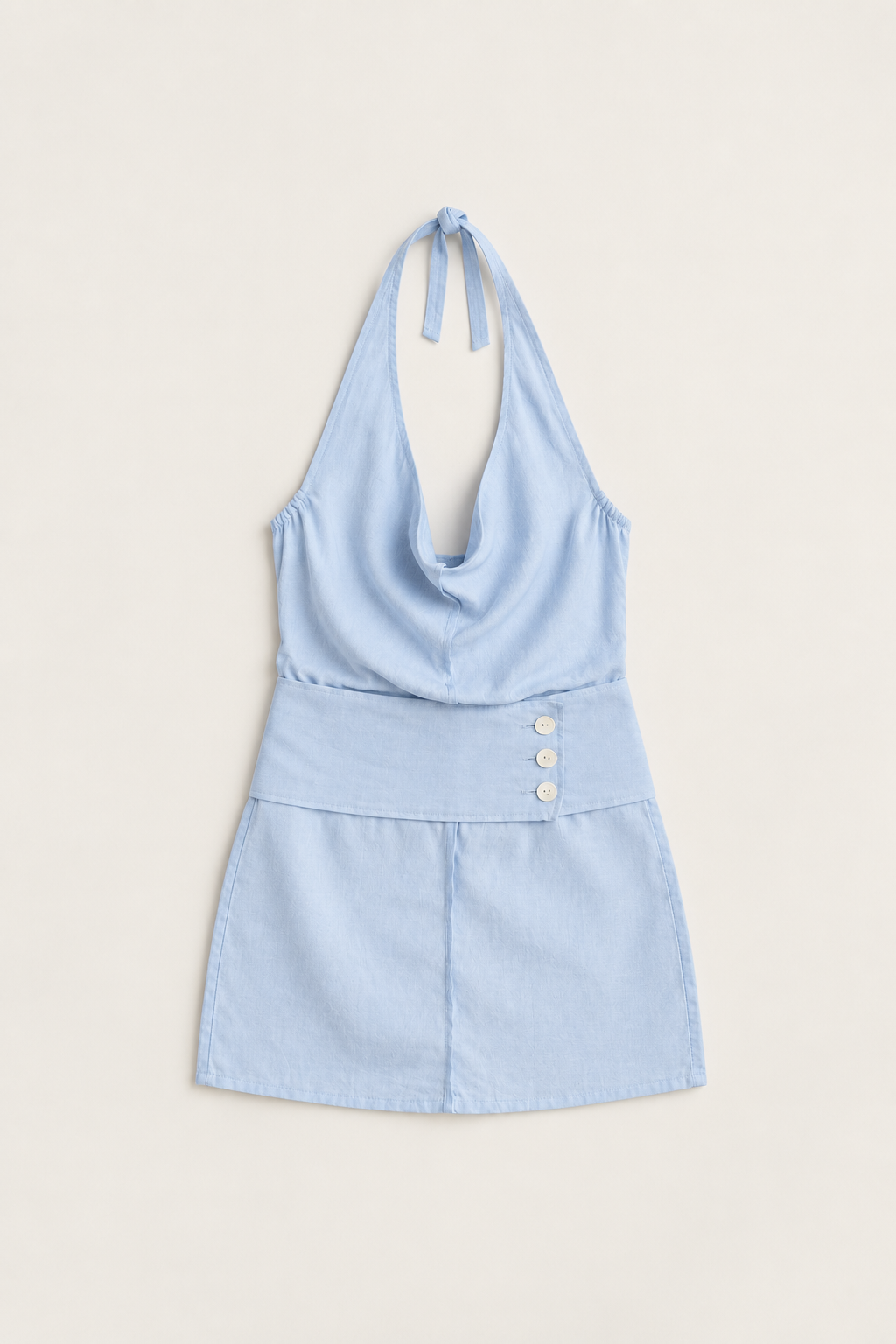 A light blue halter-neck mini dress with a wide waistband featuring three decorative buttons, laid flat against a warm off-white background.