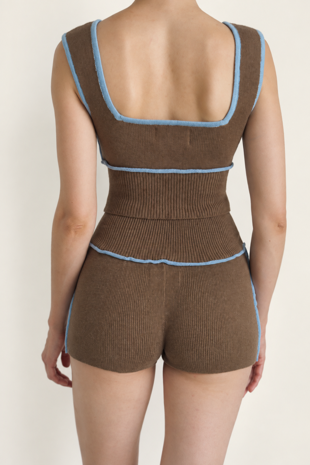 A model shown from the back wearing a brown ribbed knit one-piece romper with light blue trim details.