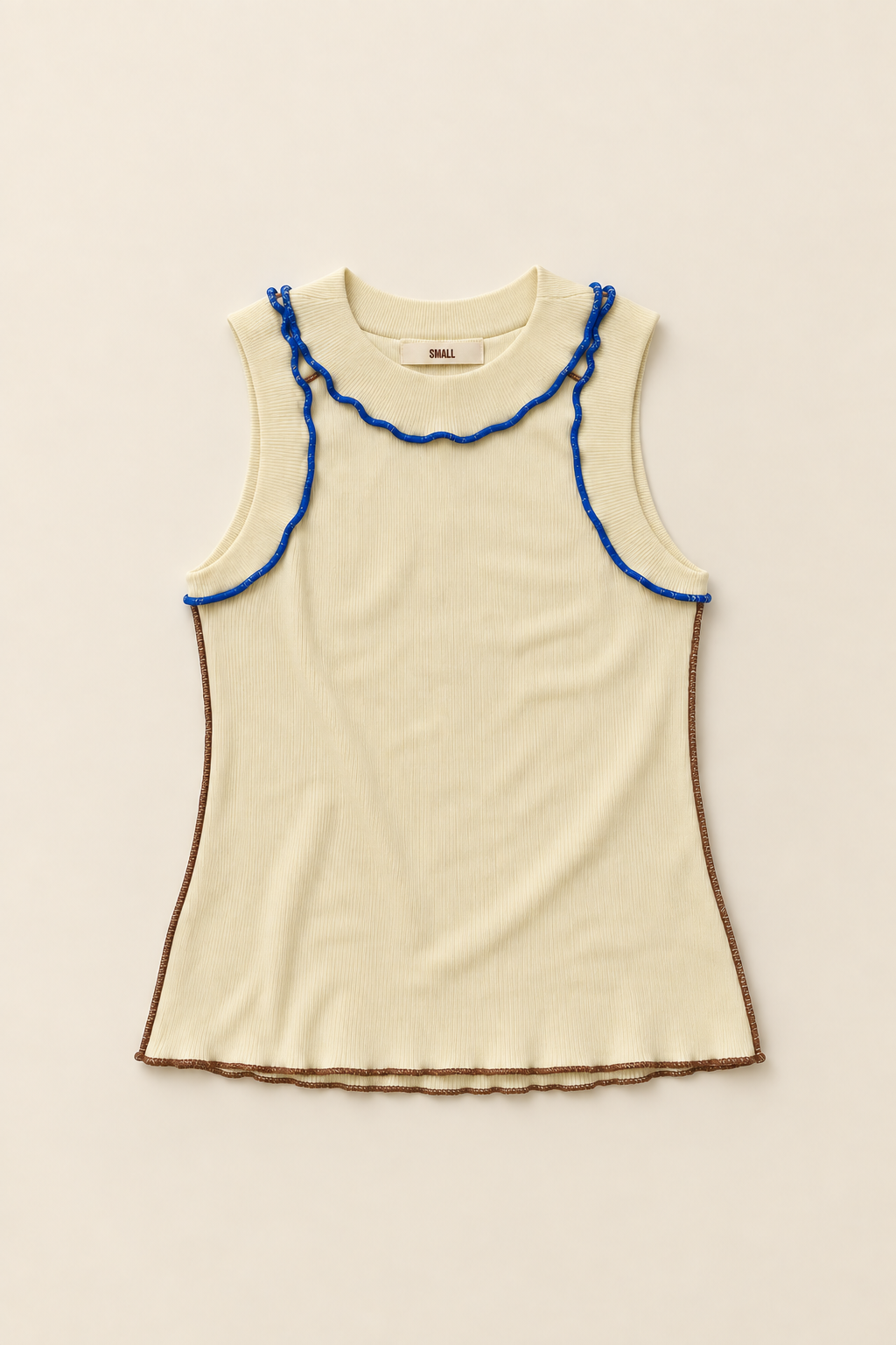A sleeveless cream knit top with blue ruffled trim along the neckline and armholes, plus a brown ruffled hem, laid flat on a light beige background.