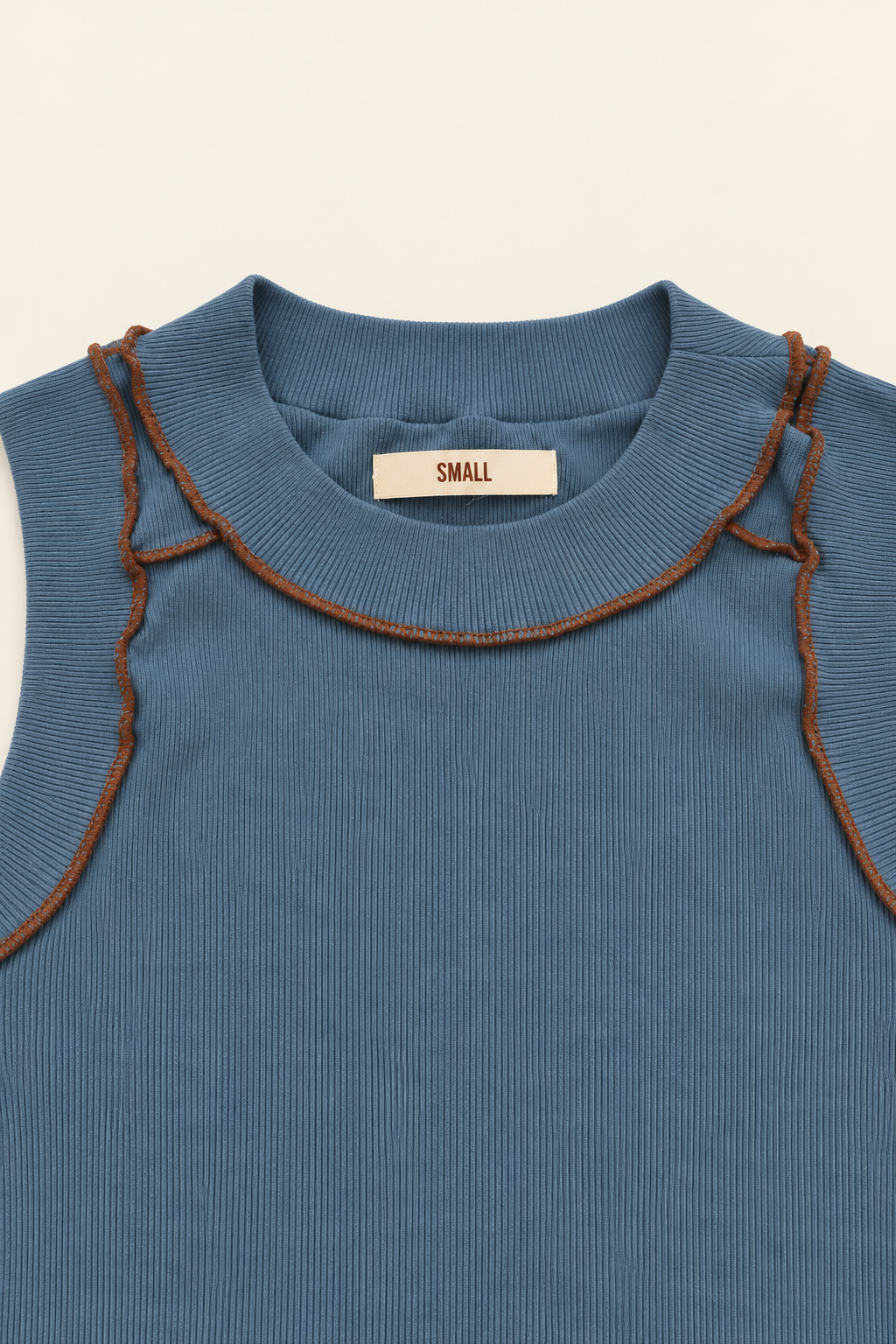 Close-up of a blue ribbed knit top with brown contrast stitching along the ruffled collar, featuring a cream label that reads 'SMALL'.